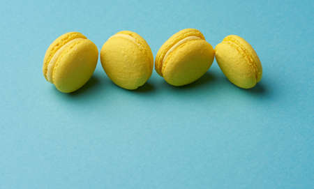 yellow lemon round baked macarons cakes on a blue background, dessert stands in a row, close up, copy spaceの写真素材