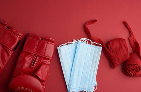 stack of disposable medical masks, a pair of leather boxing gloves and a red textile bandage, the concept of doing sports during a pandemic, top view, copy spaceの写真素材