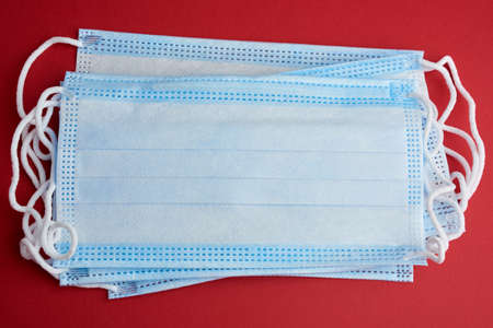 blue disposable medical mask on a red background, personal protective equipment for the respiratory tract from viral infections, top viewの写真素材
