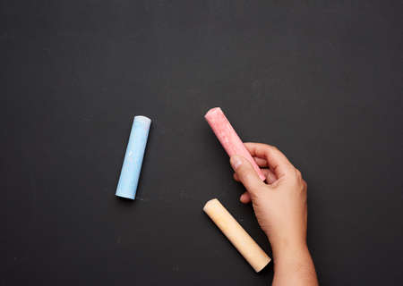 female hand holding red chalk on a background of an empty black chalk board, close upの写真素材