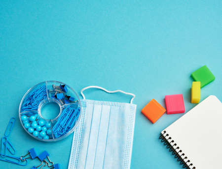 disposable medical face mask and spiral paper notebook, stationery on blue background, epidemic and...