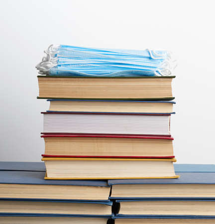 stack of various books and disposable medical masks on a white background, concept of visiting libraries in personal protective equipment during quarantineの写真素材