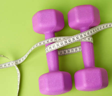pair of purple dumbbells tied with a centimeter on a green background, body weight control concept, top viewの写真素材