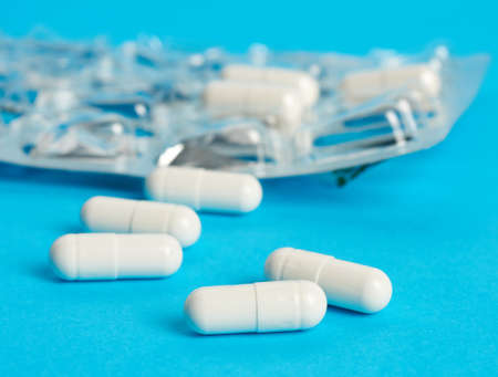 white capsules on a blue background, behind a blister pack, close up
