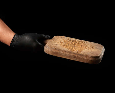 male hand in black latex glove hold an empty vintage brown wooden cutting board, black background