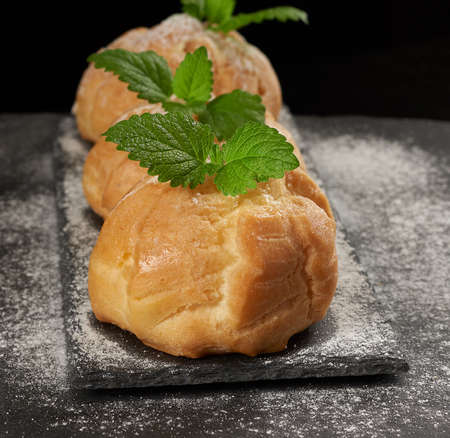 baked custard eclairs and sprinkled with powdered sugar and decorated with a mint leaf on a black board, close upの写真素材