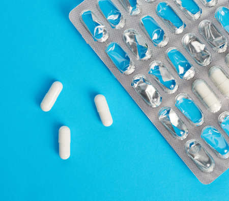 white capsules on a blue background and blister pack, close up
