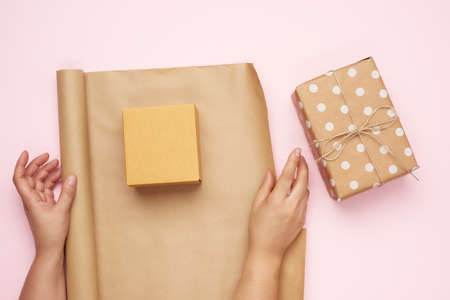 two female hands pack gifts in brown kraft paper on a pink background, top viewの写真素材