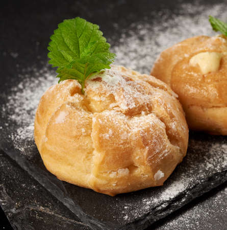baked custard eclairs and sprinkled with powdered sugar and decorated with a mint leaf on a black...