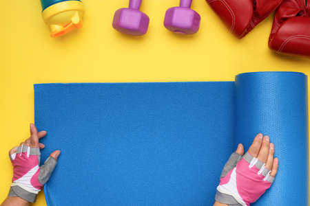 female hands in sports gloves unfold a sports mat on a yellow background, top viewの写真素材