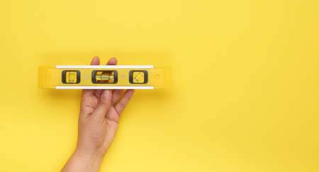 female hand hold plastic yellow level tool with capsules on a yellow background, copy space