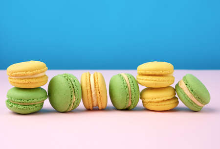 stack of yellow and green round almond flour cakes macarons with cream on a blue background,...
