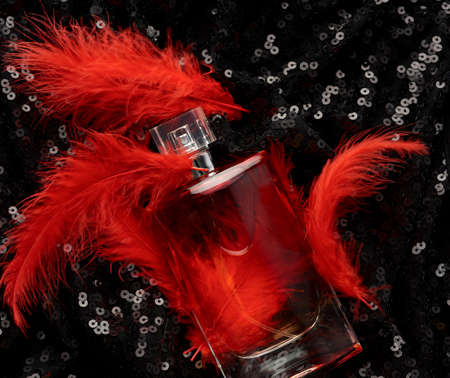 glass bottle with pink perfume liquid on black background with shiny sequins and red feathers, top viewの写真素材