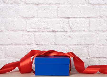 blue cardboard box with gift and red silk ribbon on white brick wall backgroundの写真素材