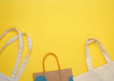 paper and empty beige textile bag on yellow background, rejection of plastic bags, flat lay, zero...