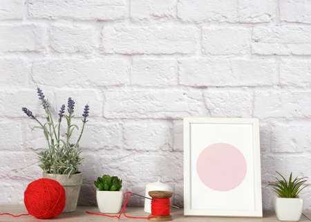 empty photo frame, succulents to a white ceramic pot and a red ball with woolen thread, white brick...