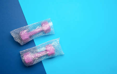 a pair of sports purple dumbbells in a transparent bag on a blue background, top view, copy space