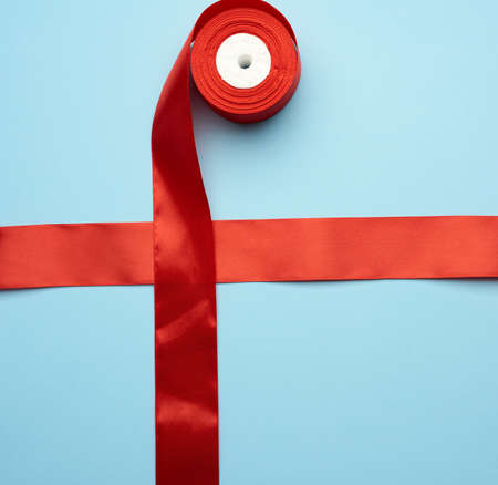 red silk ribbon crossed on a blue background, tying a gift, top viewの写真素材