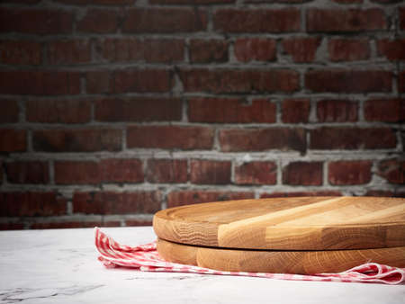 empty round wooden cutting board against brown brick wall background and red kitchen towelの写真素材