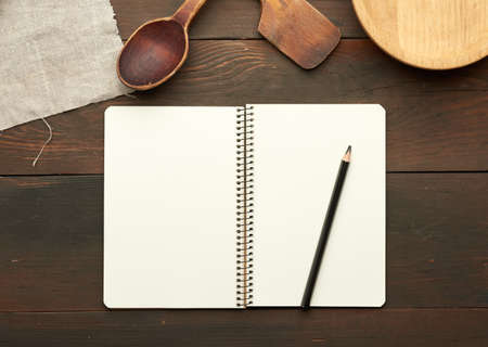 open notebook with blank white sheets and kitchen utensils on brown wooden table, top viewの写真素材