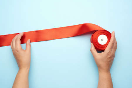 two female hands and red silk ribbons on a blue background, top viewの写真素材