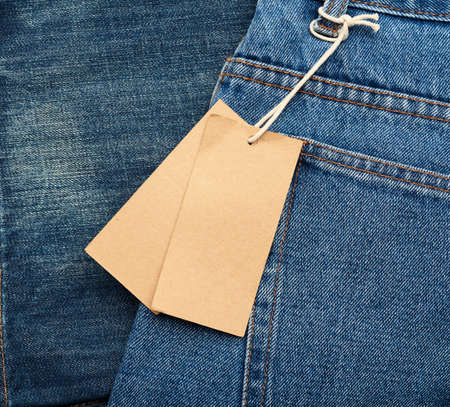 blank brown rectangular tag tied in the back pocket of blue folded jeans, close upの写真素材