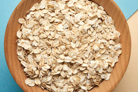 raw oatmeal in a brown wooden bowl on a blue background, top view