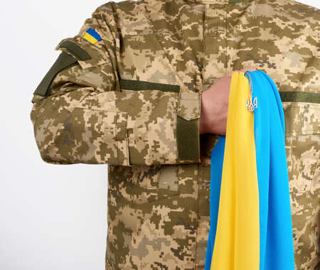 Ukrainian man warrior dressed in a military pixel uniform holds the yellow-blue flag of the state of Ukraine and on the chain a small coat of arms of the country of trident, white backgroundの写真素材