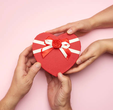male hands give a red box with a gift to a woman, top view, pink background