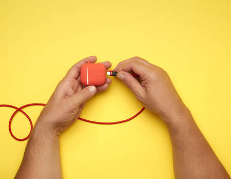 two male hands are holding a cable and a red box with wireless headphones, yellow table, top viewの写真素材
