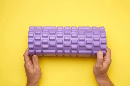two male hands hold purple massage roll for back and body on yellow background, top viewの写真素材