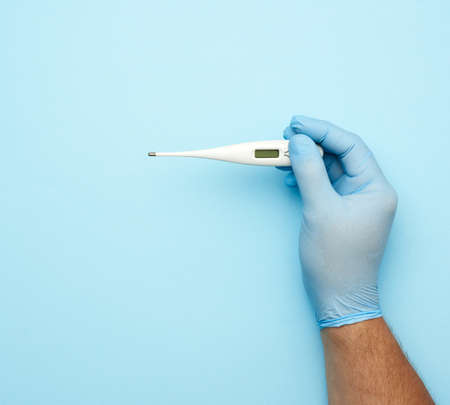 male hand in a blue medical glove holds a white plastic thermometer, blue backgroundの写真素材