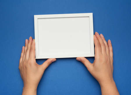 two female hands holding a rectangular blank white frame, blue backgroundの写真素材
