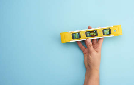 female hand hold plastic yellow level tool with capsules on a blue background, copy space