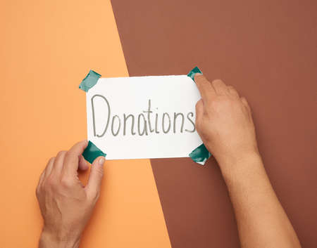 two male hands hold a sheet of paper with the inscription donations, brown background