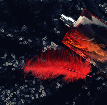 glass bottle with pink perfume liquid on black background with shiny sequins and red feathers, top viewの写真素材