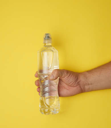 transparent plastic bottle with fresh water in a male hand on a yellow background, close up