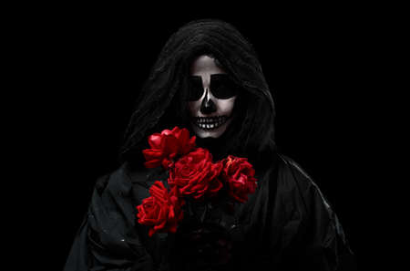 woman in a black hood with a skeleton make-up holds a bouquet of red roses in front of her, an invented image for the Halloween holidayの写真素材