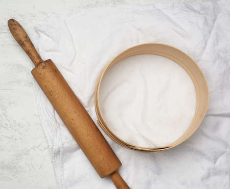 vintage wooden rolling pin and a round sieve lie on a white linen napkin, top view