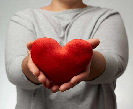 female hand holds a red textile heart, white background. Love and donation concept