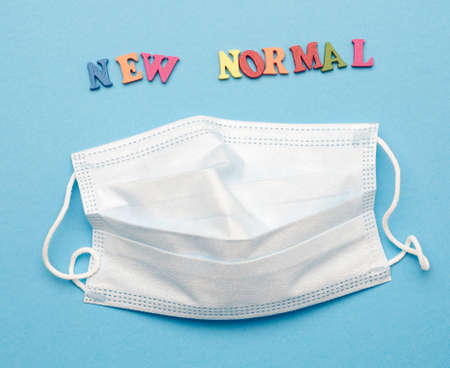 disposable medical face mask and lettering new normal on blue background, concept of wearing...