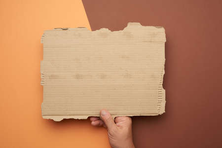 male hand hold a blank torn piece of brown paper, brown backgroundの写真素材