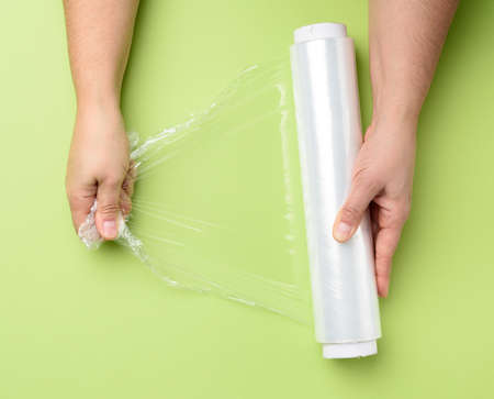 two female hands hold a roll of transparent cling film for packaging products, green backgroundの写真素材