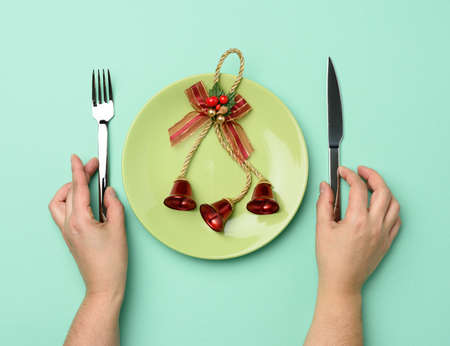 round green ceramic plate, two hands holding a knife and fork on a green background, festive table...