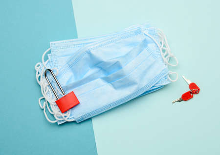 disposable mask and a metal lock on a blue background, daily life during quarantine and pandemicの写真素材