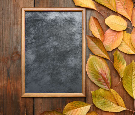 empty wooden chalk board on a brown wooden background and yellow cherry leaves, place for an...