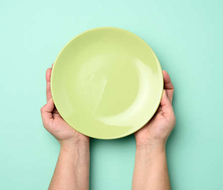 two hands holding a round empty green plate, top viewの写真素材