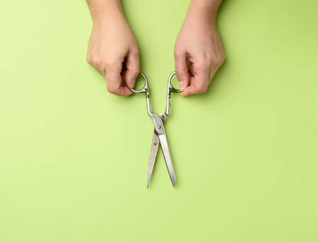 female hand holding vintage metal scissors on green background, close upの写真素材