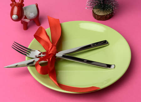 round green plate and metal fork and knife tied with a red silk ribbon, pink backgroundの写真素材