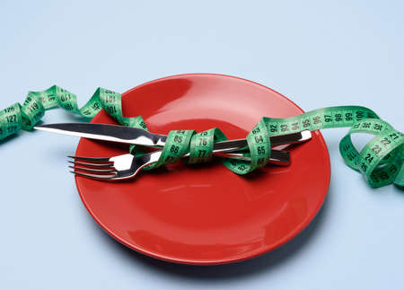 fork and knife wrapped in green measuring tape on blue background, weight loss concept, flat layの写真素材